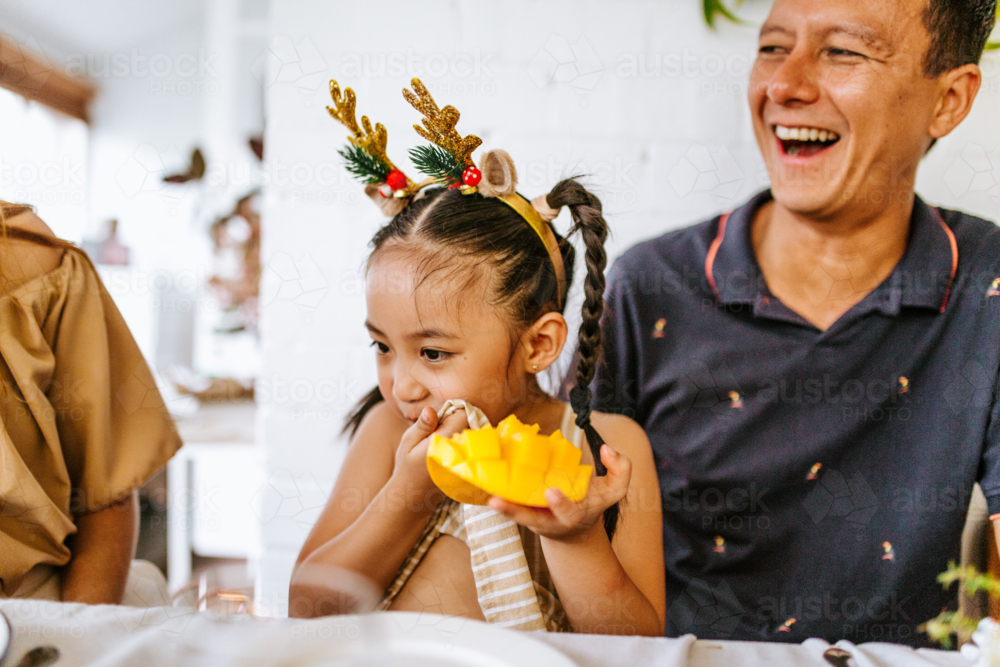 Young girl wiping her mouth while holding ripe mango. - Australian Stock Image