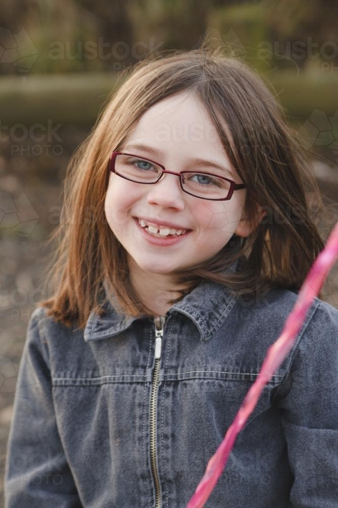 Young girl with glasses and jacket smiling at camera - Australian Stock Image