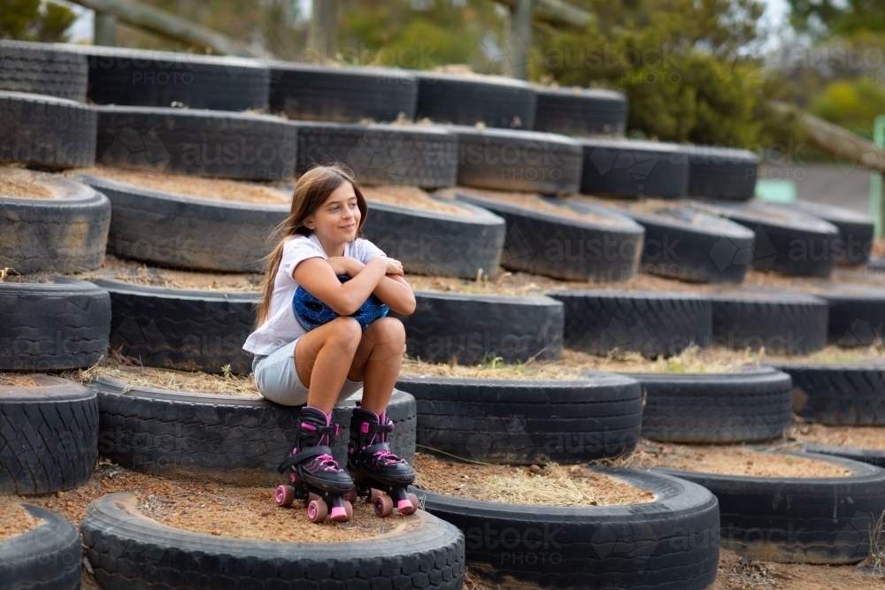 young girl with long hair sitting outdoors wearing roller skates - Australian Stock Image