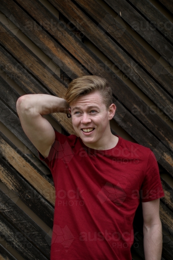 Young happy caucasian man modelling in front of a wooden panelled background - Australian Stock Image