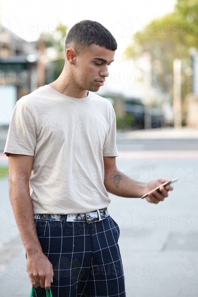 Young Indigenous Australian man looking at mobile phone outdoors - Australian Stock Image