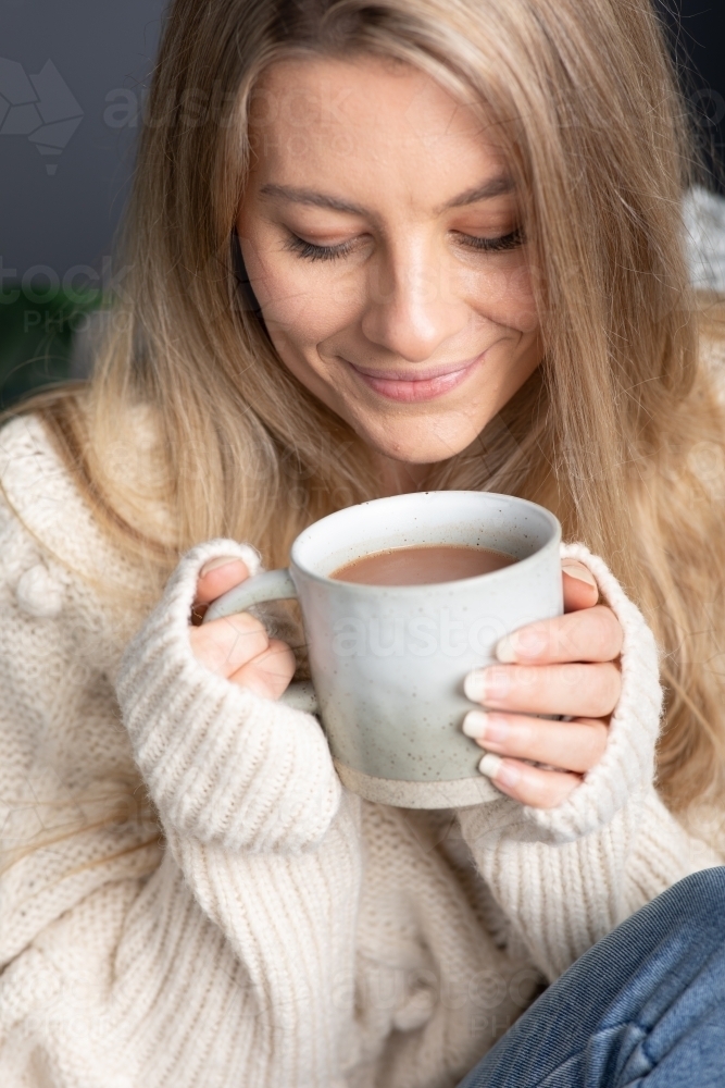 Young lady relaxing drinking hot chocolate or coffee on a cold winters day - Australian Stock Image