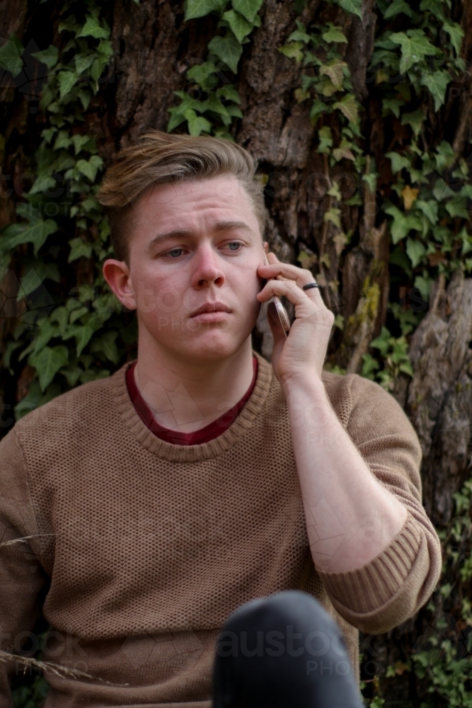 Young male sitting outside using mobile phone - Australian Stock Image