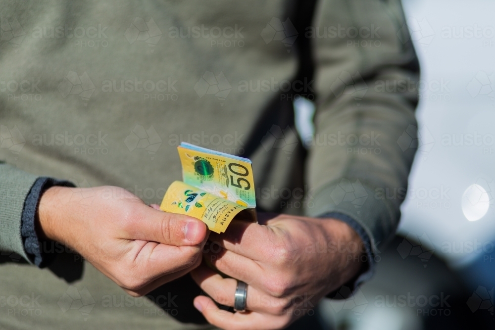 Young man holding cash standing in front of car paying up front - Australian Stock Image