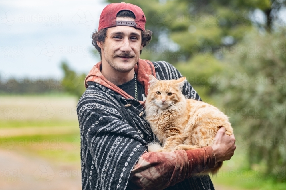 Young man holding pet cat outdoors. - Australian Stock Image