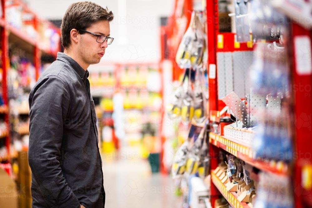 Young man in hardware store looking at tools - Australian Stock Image