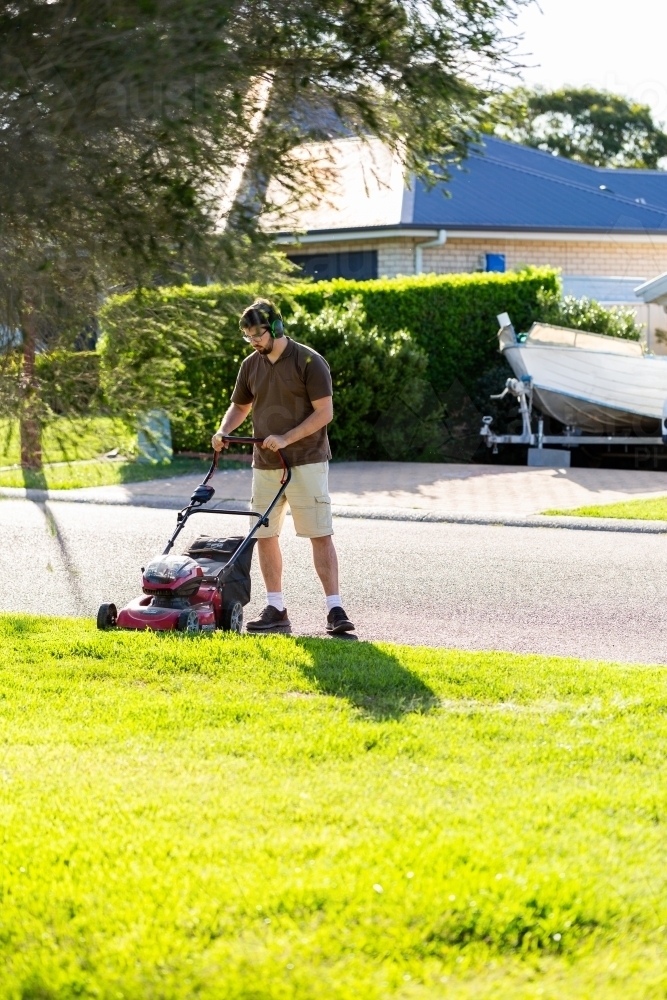 Young man mowing front lawn with push mower - Australian Stock Image