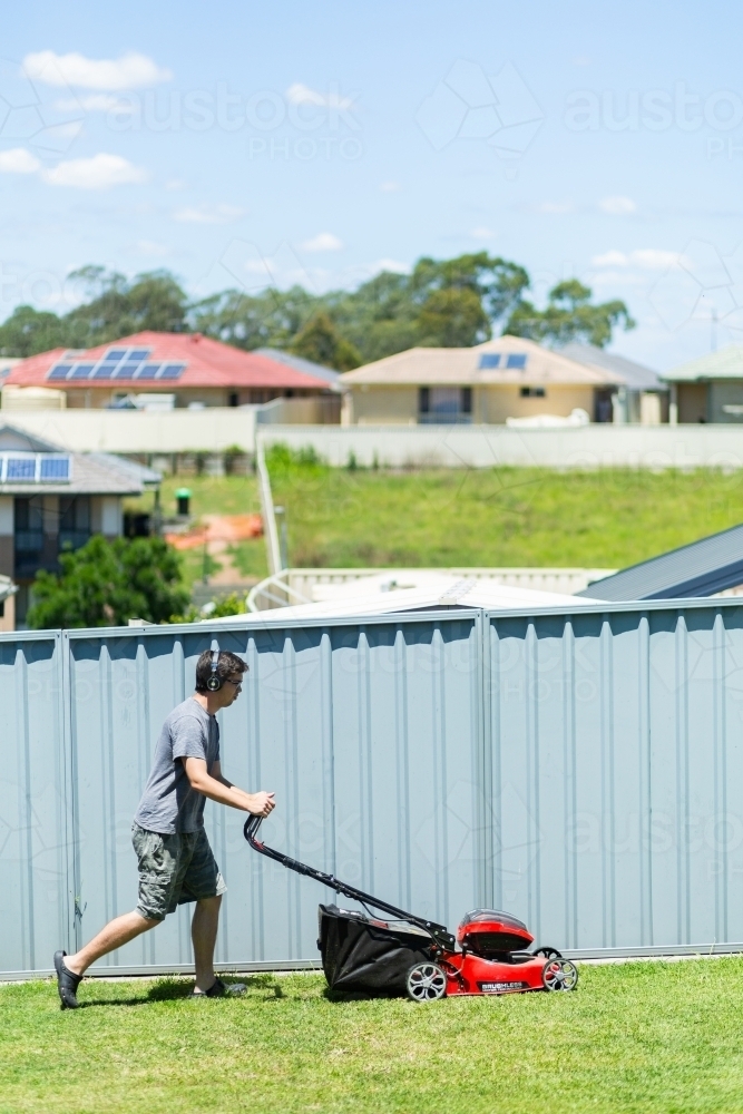 Young man mowing grass in suburban backyard with a push mower - Australian Stock Image