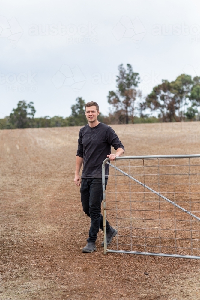 Young man opening a gate on a country property - Australian Stock Image