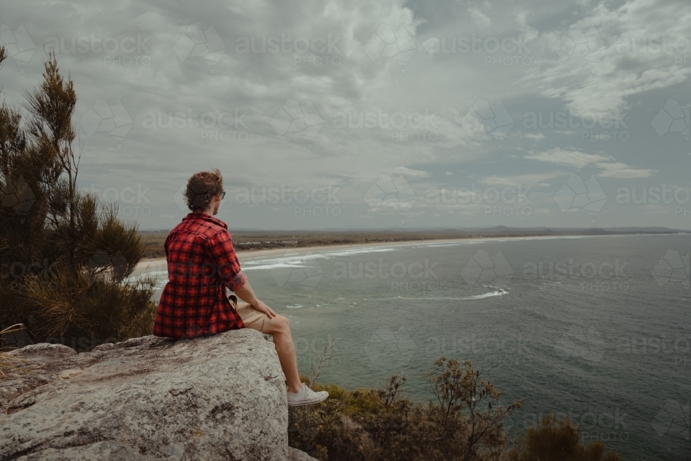 Young man relaxing at a lookout overlooking the beach and ocean at Evans Head. - Australian Stock Image