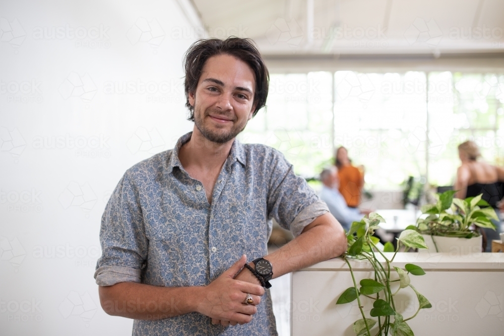 Young man standing, smiling in white office - Australian Stock Image