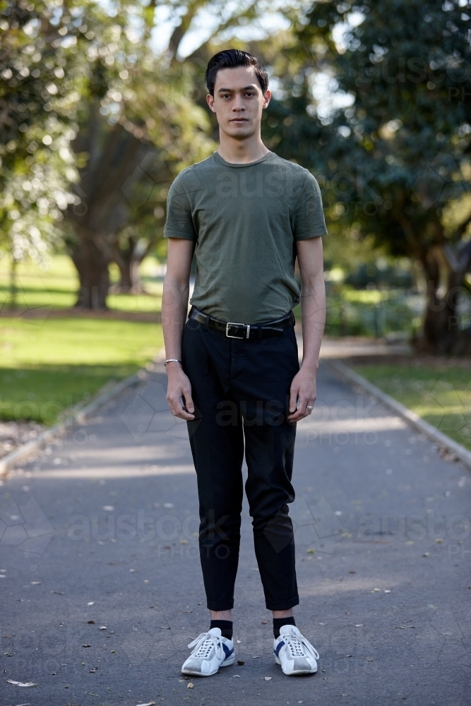 Young man with dark hair standing outside at park - Australian Stock Image