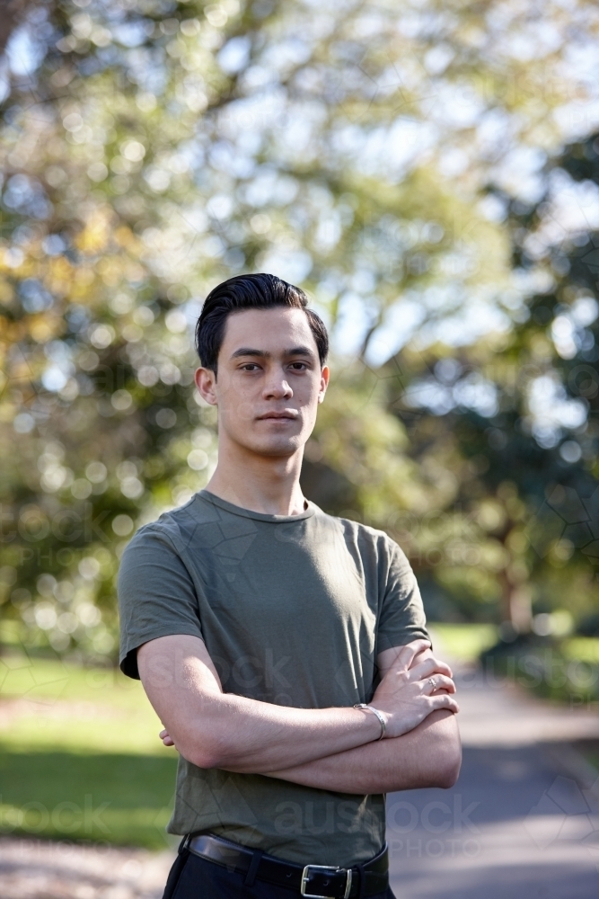 Young man with dark hair standing outside at park - Australian Stock Image