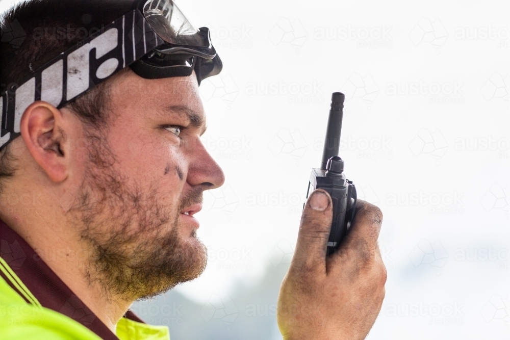 Young man with dirty face taking on walky-talky two way radio - Australian Stock Image