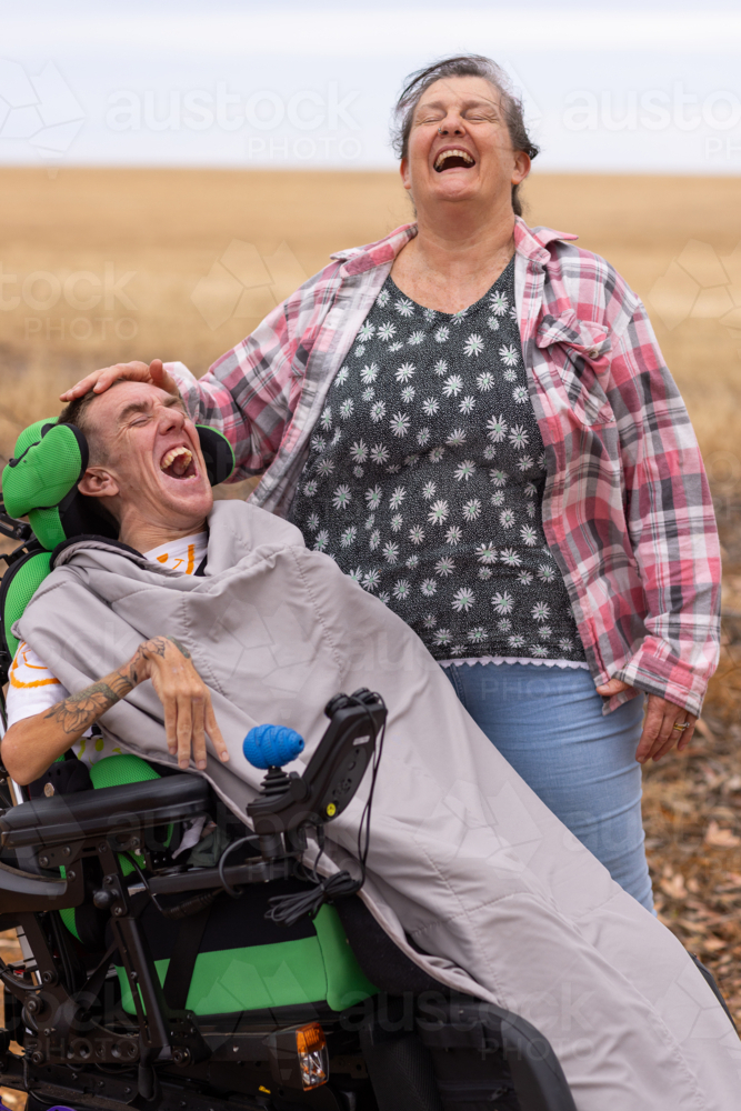 Young man with disability laughing with mother standing on dirt road in country - Australian Stock Image