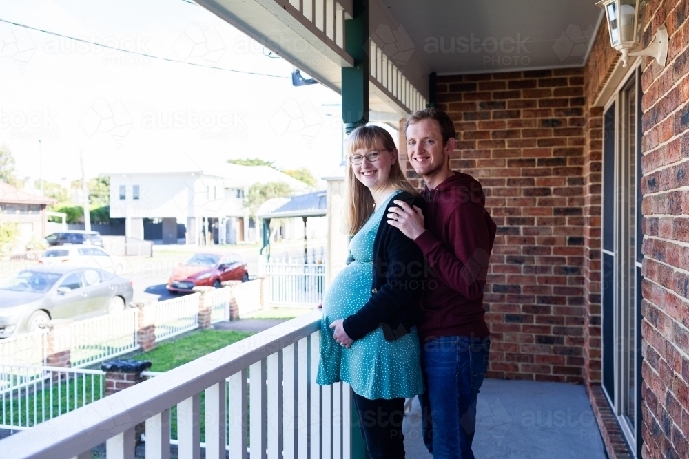 Young married couple with baby on the way standing on verandah of rental home - Australian Stock Image