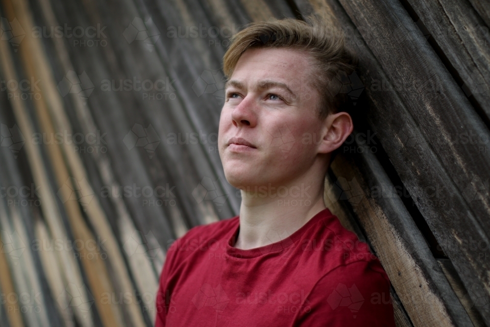 Young melancholy caucasian man modelling in front of a wooden panelled background - Australian Stock Image