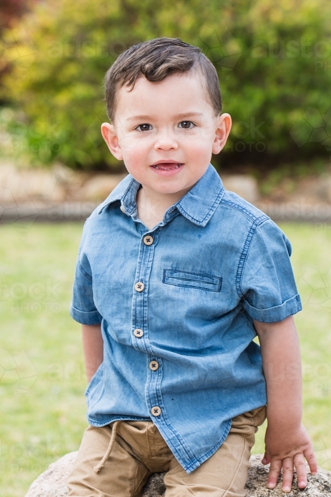 Young mixed race aboriginal caucasian boy sitting on rock smiling - Australian Stock Image