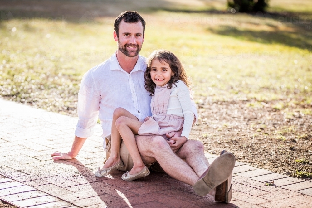 Young mixed race Aboriginal girl sitting on Caucasian father's lap - Australian Stock Image