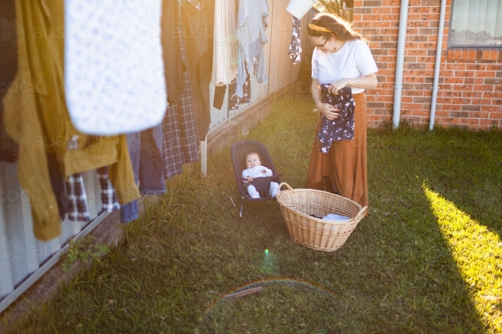 image-of-young-mum-folding-washing-in-backyard-with-baby-in-bouncer