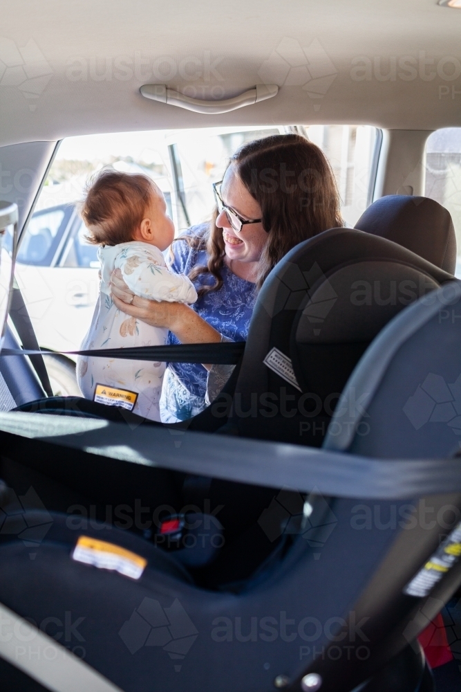 Young parent lifting baby out of rear facing child car seat - Australian Stock Image