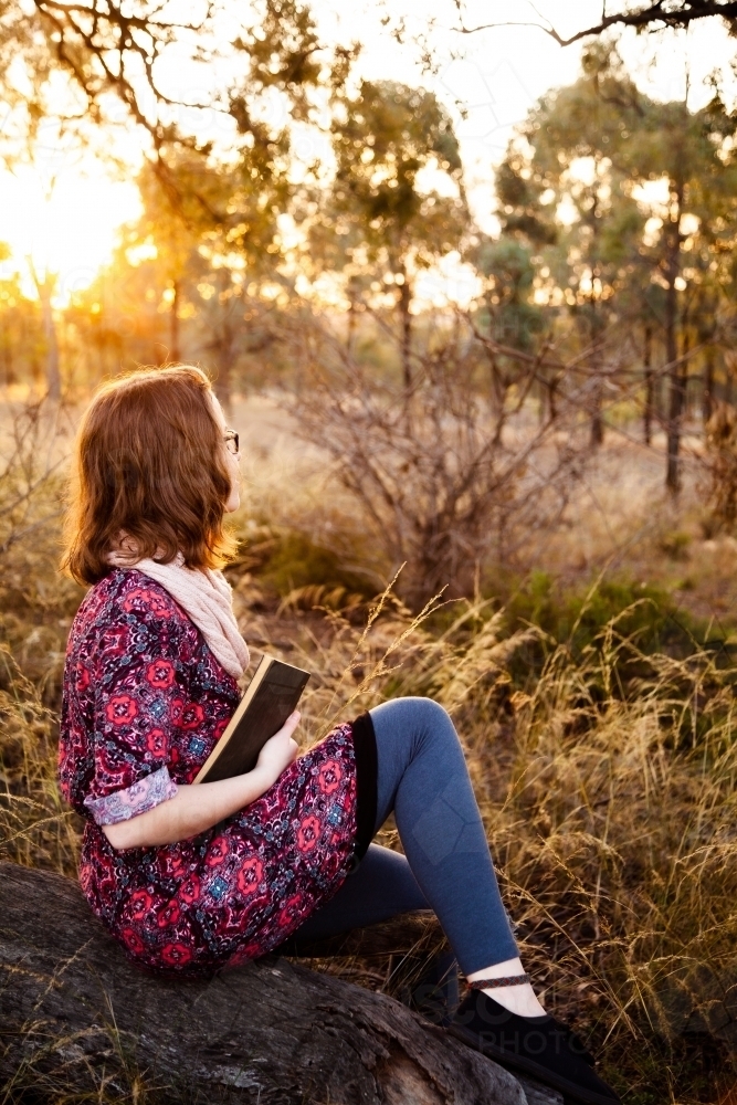 Young person holding a notebook looking away, outside in nature - Australian Stock Image