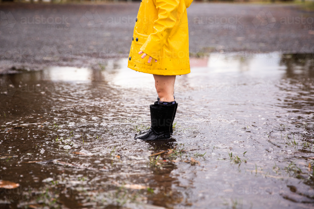 young person in gumboots and jacket in a puddle - Australian Stock Image