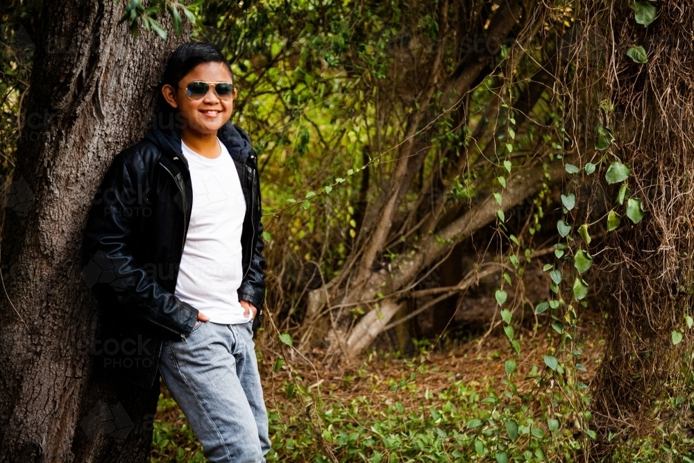 Young person leaning on tree in overgrown bushland with copy space - Australian Stock Image