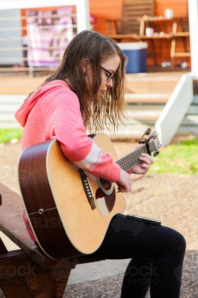 Young person playing guitar outside sitting on park bench - Australian Stock Image