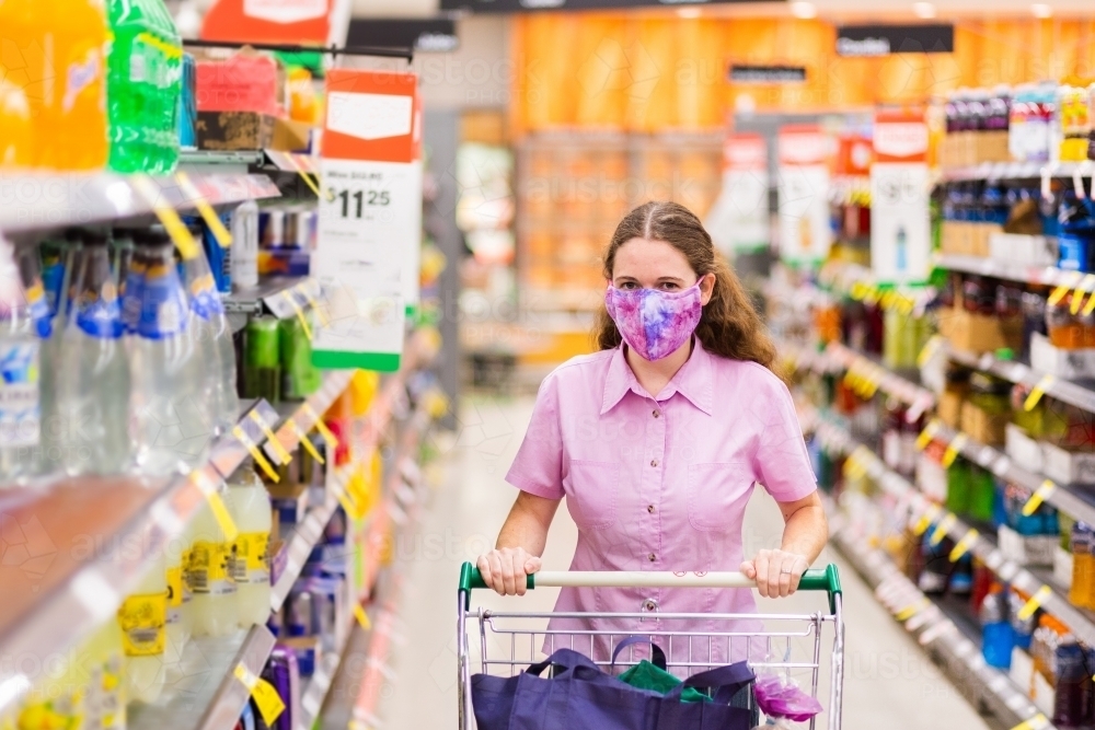 Young person walking down grocery store aisle wearing home made face mask during covid-19 pandemic - Australian Stock Image