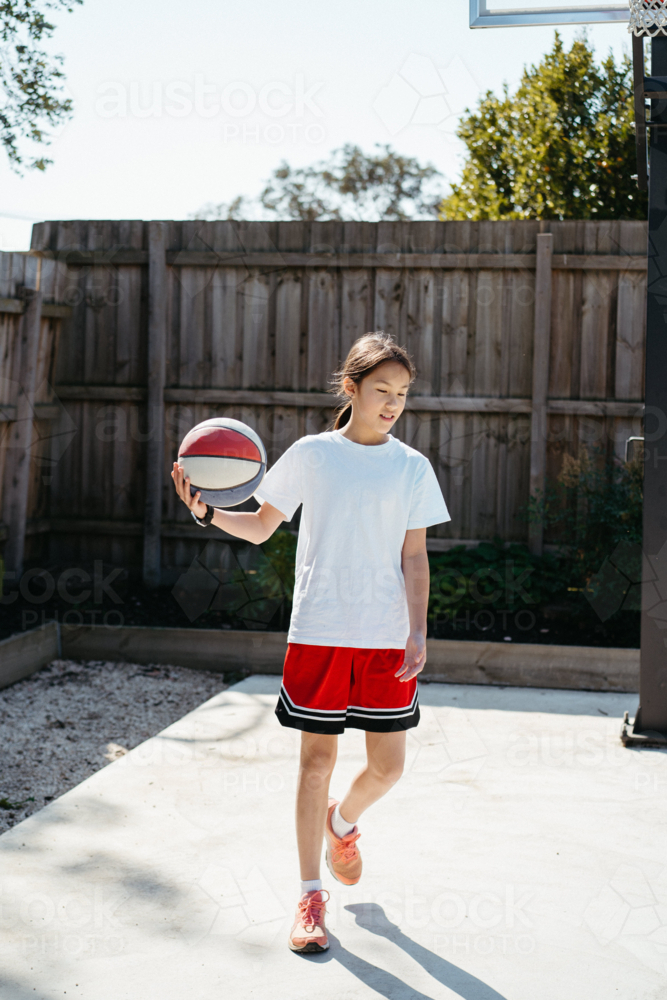 Young pre-teen girl playing basketball in the backyard - Australian Stock Image