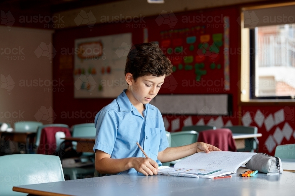 Young school boy in classroom working on homework - Australian Stock Image