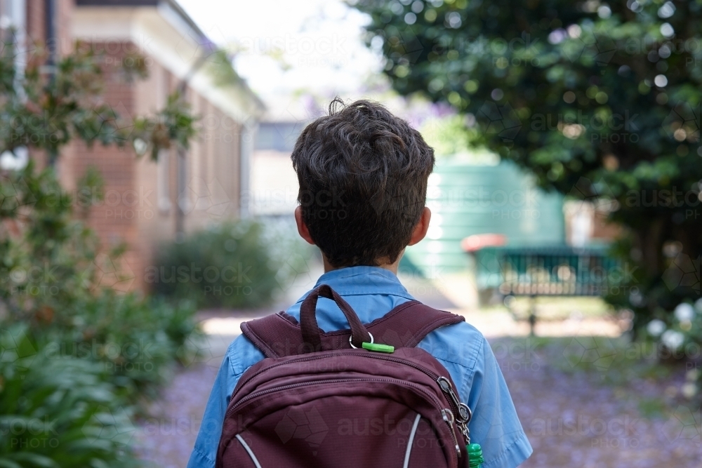 Young school boy walking away from camera, to class - Australian Stock Image