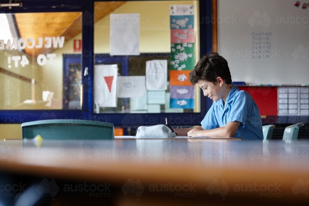 Young school boy writing in classroom - Australian Stock Image