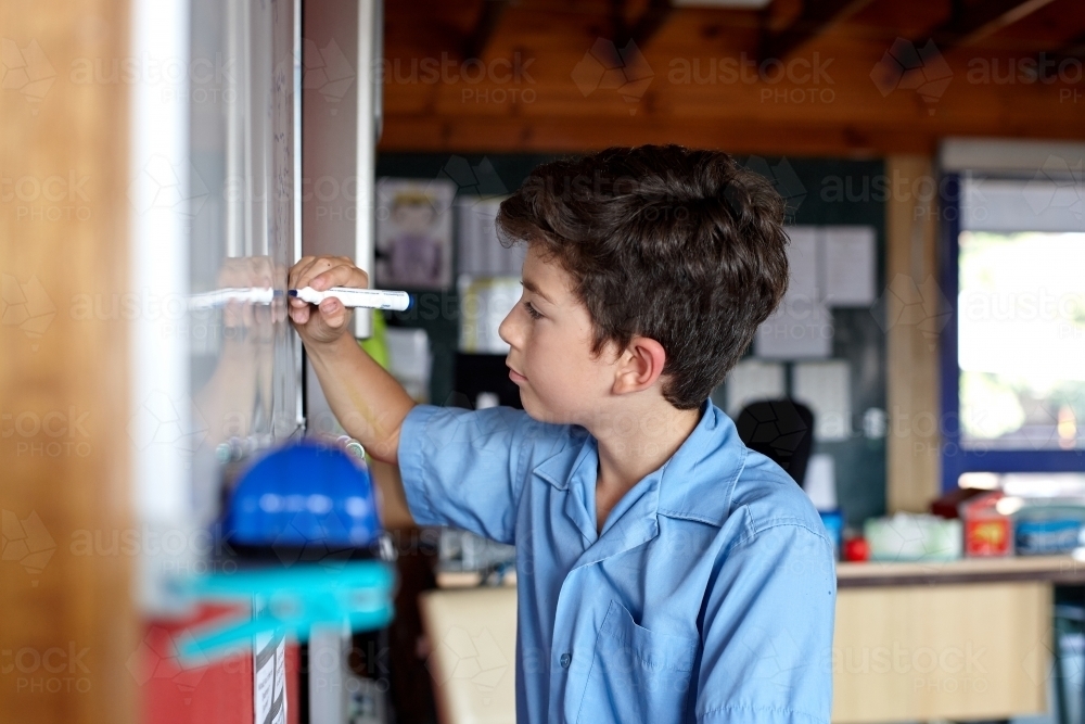 Young school boy writing on a white board in classroom - Australian Stock Image