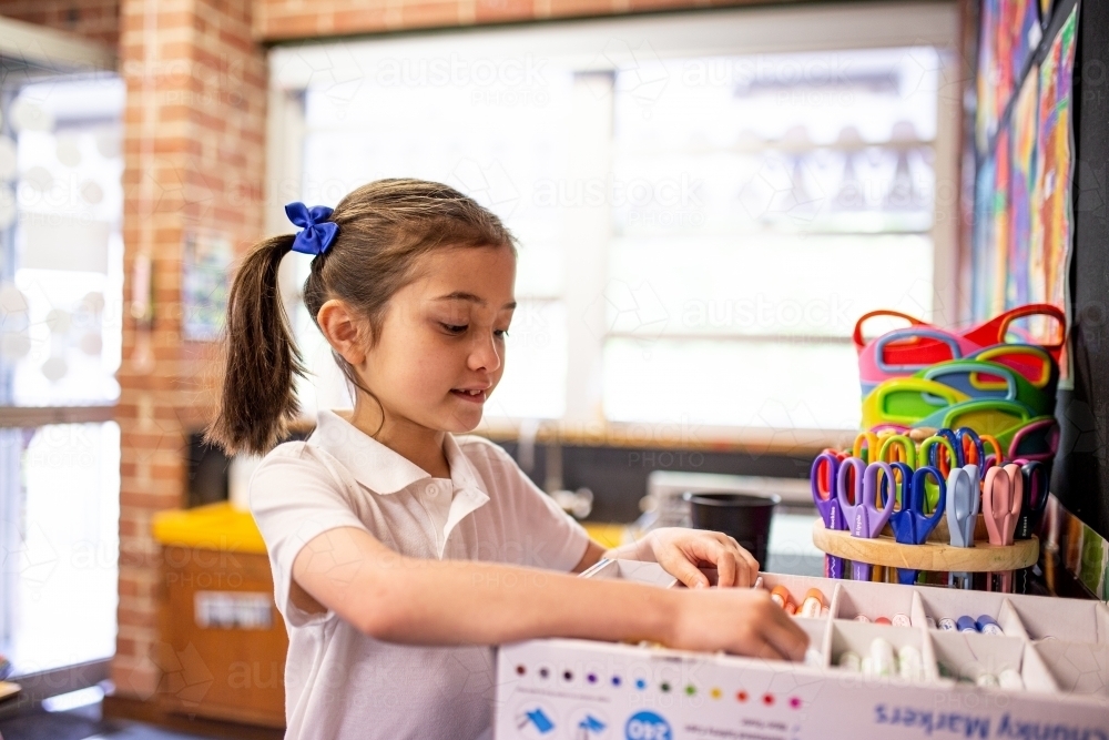 Young Schoolgirl Packing Away art supplies in a Classroom - Australian Stock Image