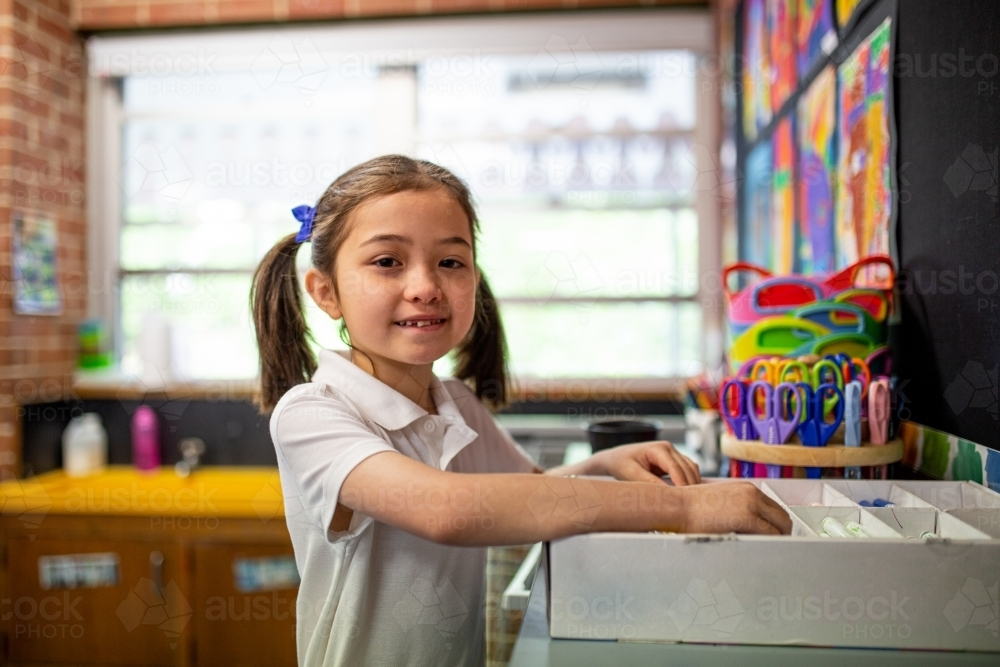Young schoolgirl standing inside the classroom smiling at camer - Australian Stock Image