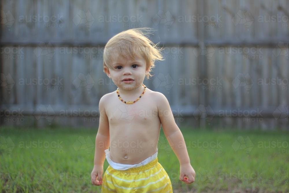 Young shirtless toddler playing in yard with wind blowing hair - Australian Stock Image