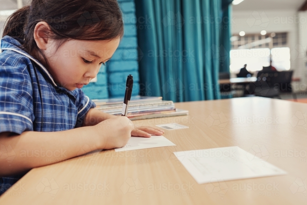 Young student girl writing in libary - Australian Stock Image