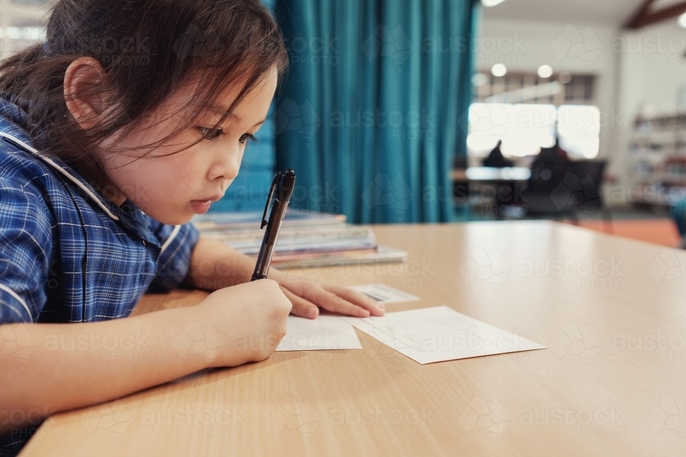 Young student girl writing in libary - Australian Stock Image