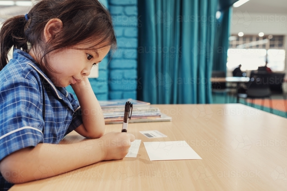 Young student girl writing in libary - Australian Stock Image