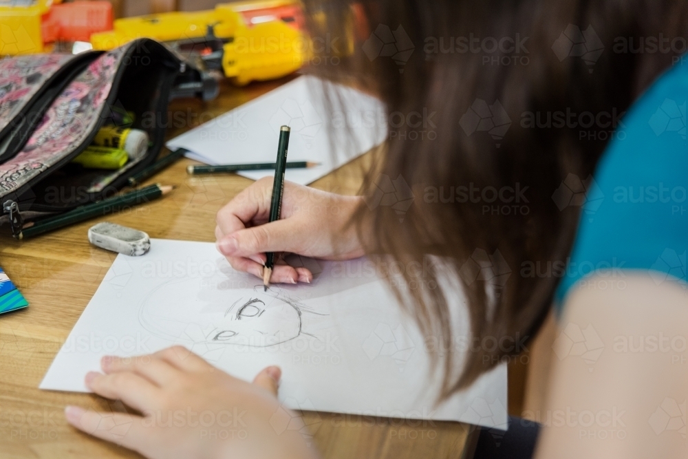Young teenage girl creating artwork, drawing Manga and stencilling at the table - Australian Stock Image