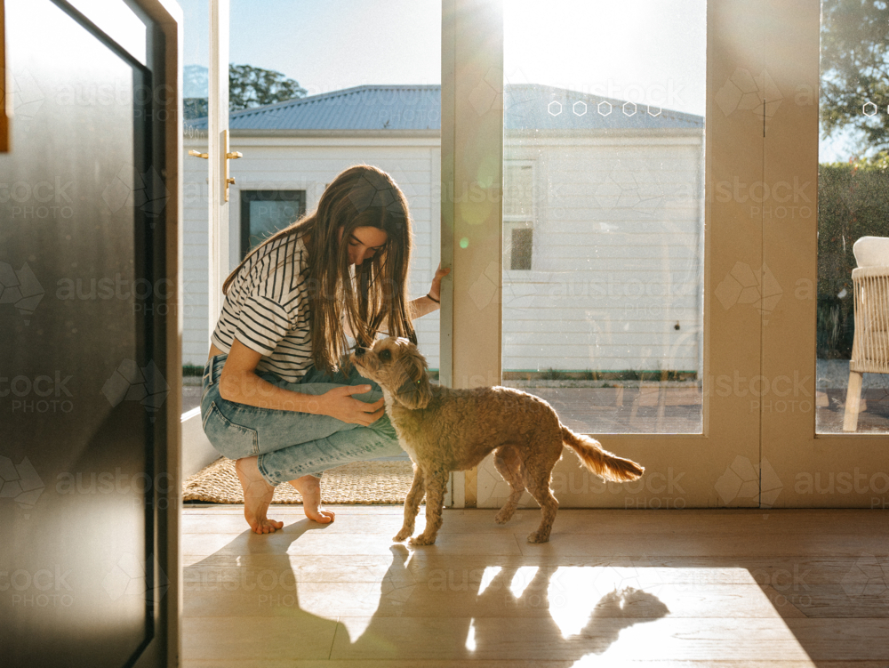 Young teenage girl petting a small dog in the doorway. - Australian Stock Image