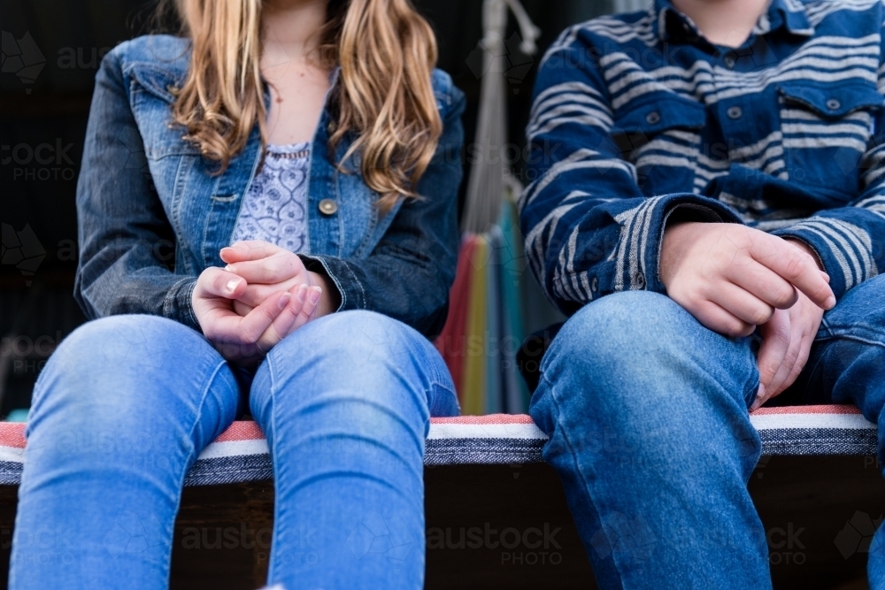 young teens sitting in a cubby house in the woods, focus on jeans - Australian Stock Image