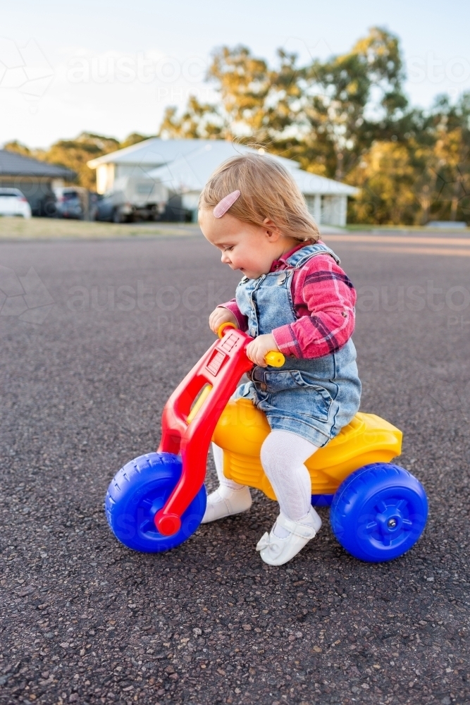 Young toddler girl riding on dune buggy tricycle on quiet urban road - Australian Stock Image