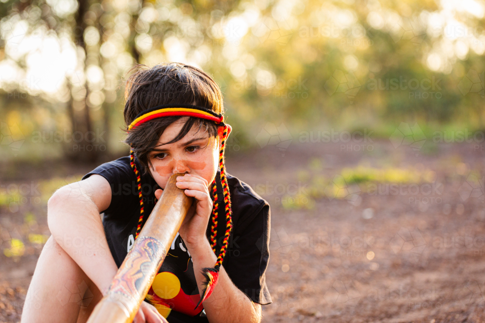 Young tween Aboriginal boy outside in rural Australia playing didgeridoo on country - Australian Stock Image