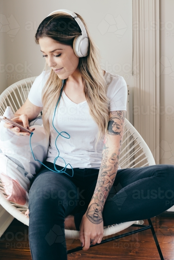 Young woman at home with headphones connected to her smartphone - Australian Stock Image