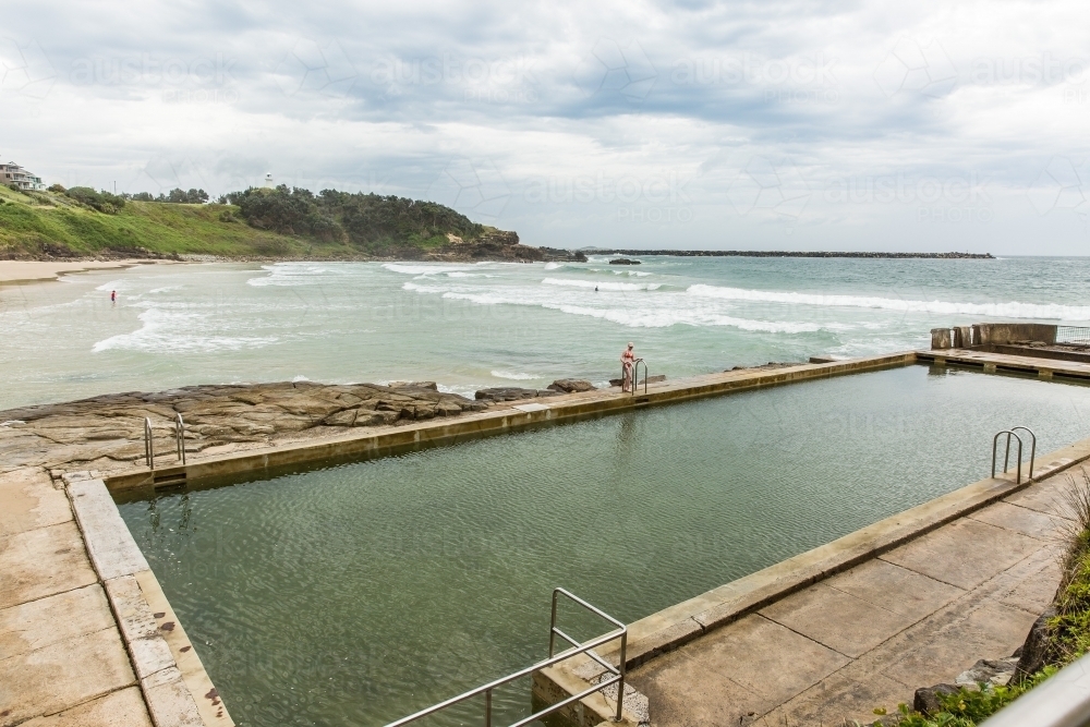 Young woman at ocean pool next to beach with cloudy skies - Australian Stock Image