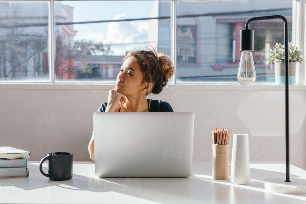 Young woman contemplating something in front of a laptop - Australian Stock Image