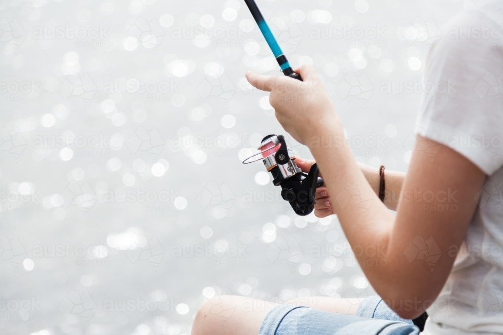 Young woman holding a fishing rod with out of focus water background - Australian Stock Image